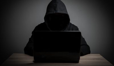 Hacker work front of his laptop computer with dark face.